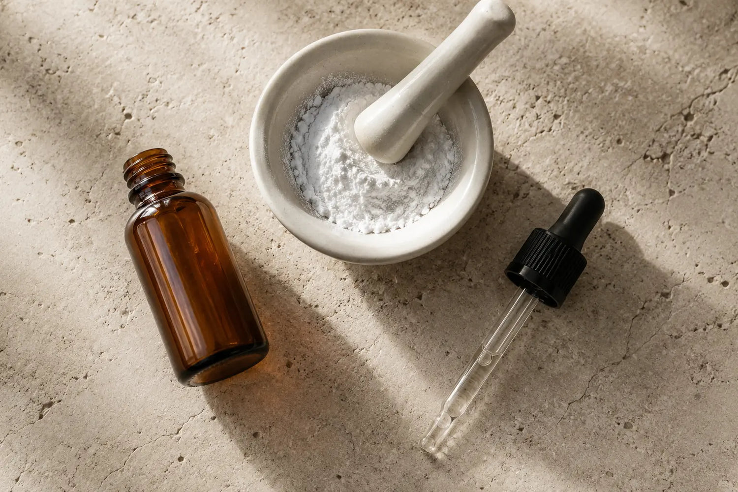 Amber glass dropper bottle and white cosmetic powder in mortar on textured stone surface — Kalós Cosmetics South Africa